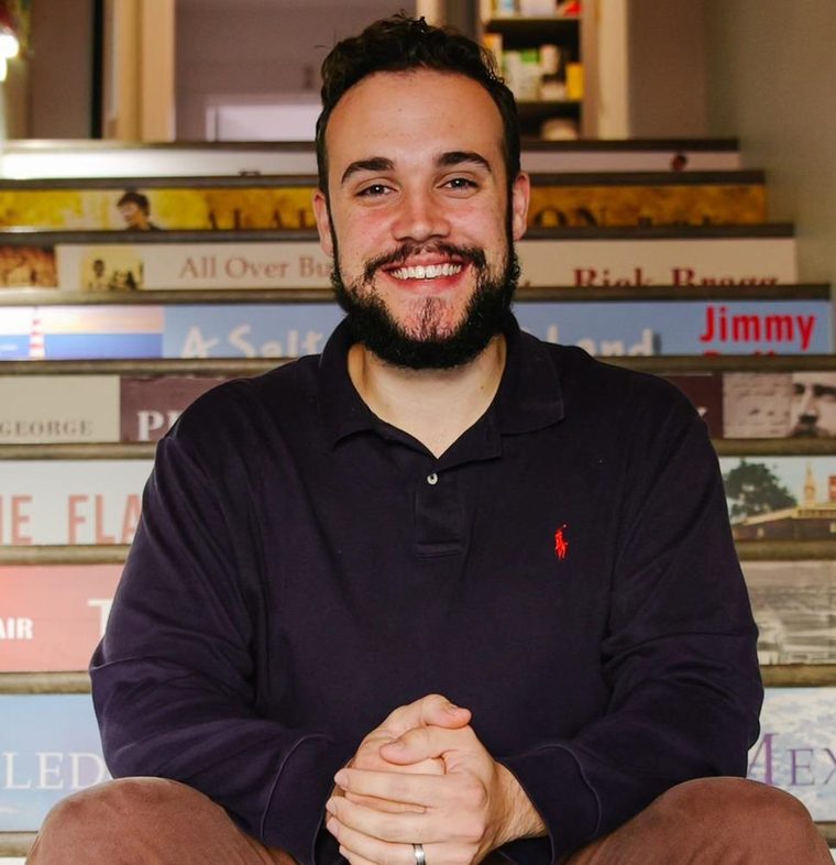 Zach Wilson, seated in front of shelves of stacked books.